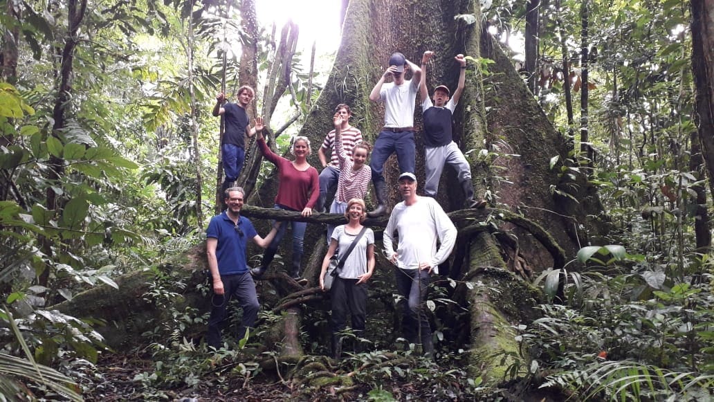 Group of tourists stand before a giant tree in the Amazon jungles of the Cuyabeno Wildlife Reserve
